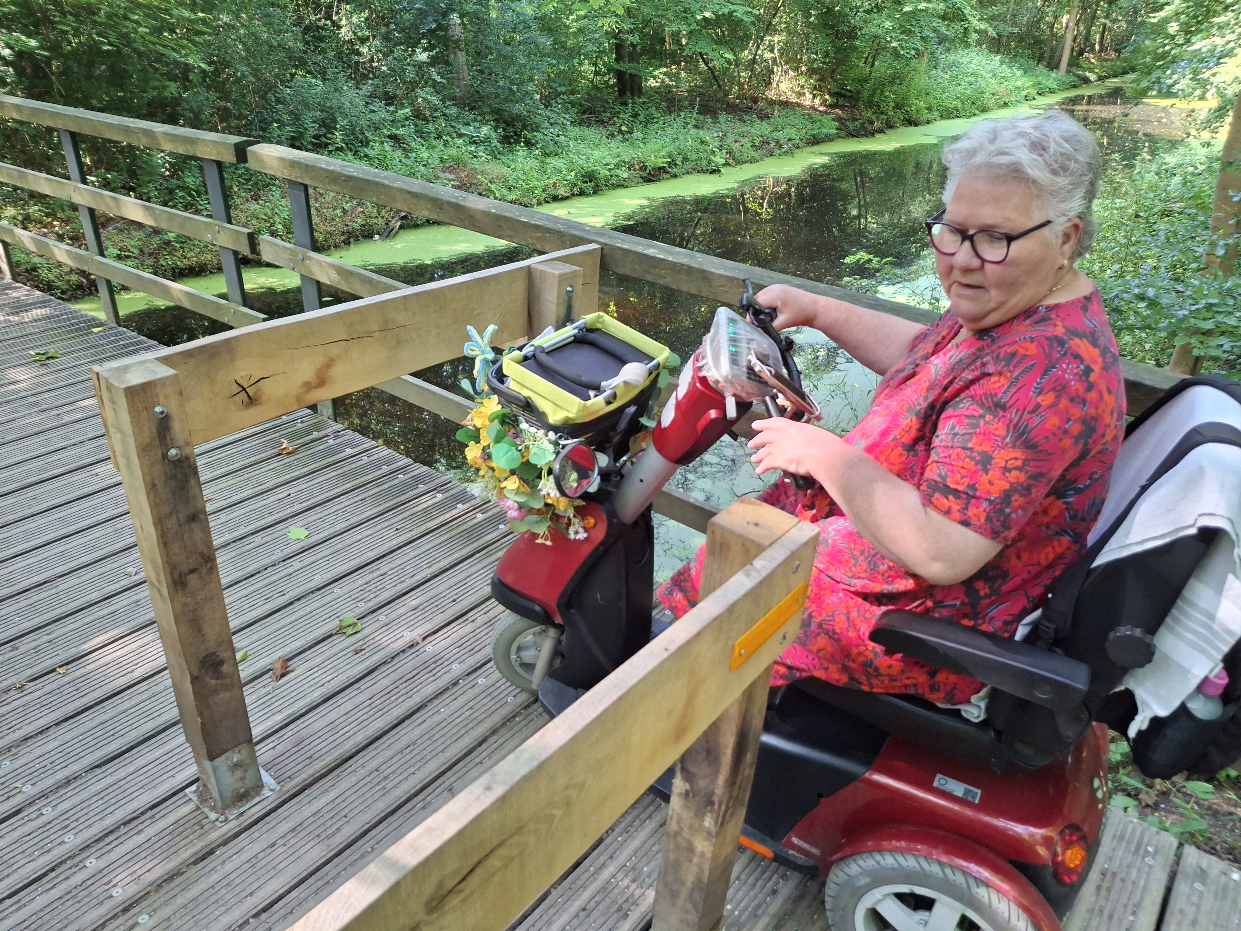 Mevrouw in scootmobiel voor een poortje waar ze niet doorheen kan.